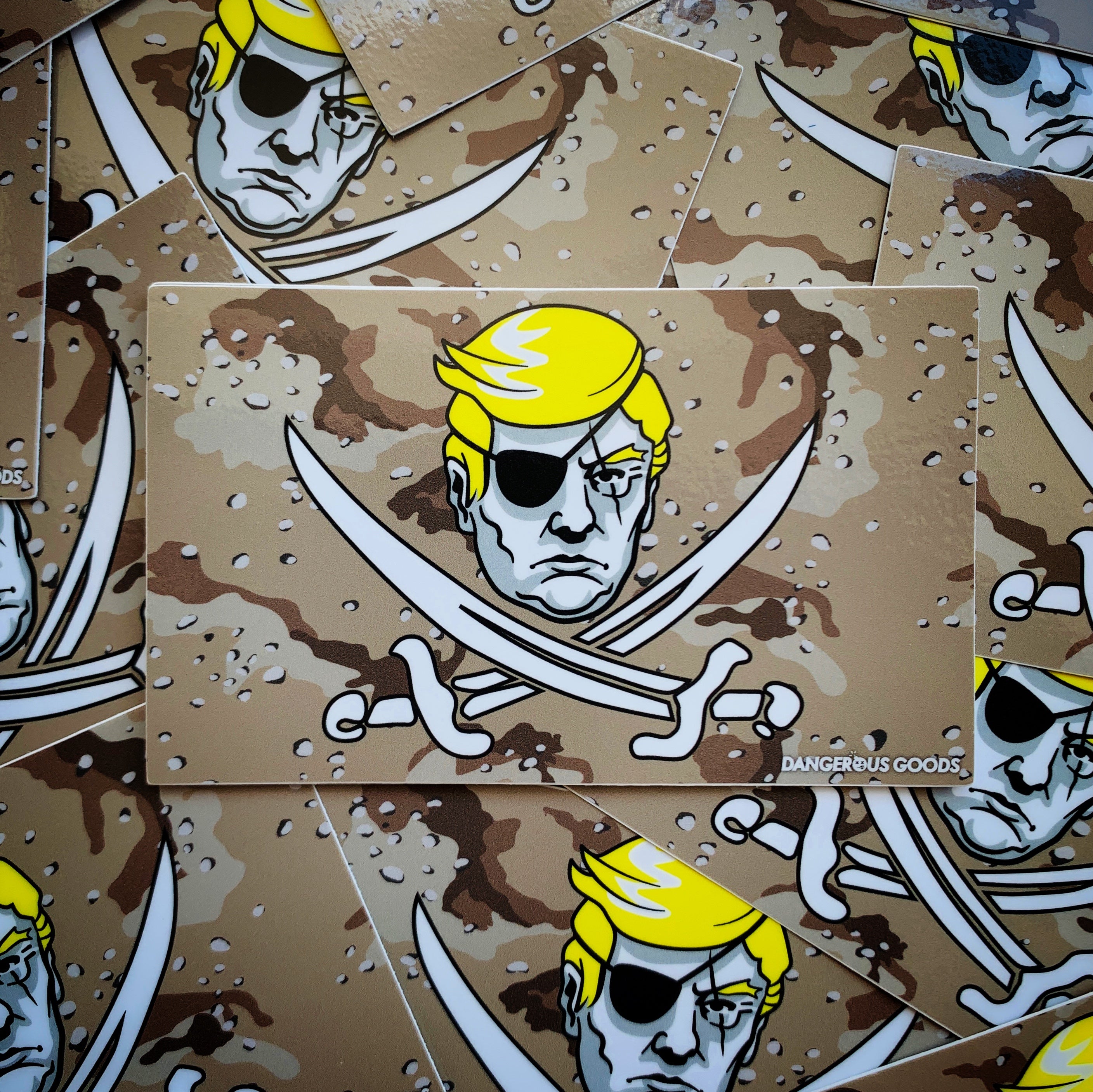Tan desert storm style camo flag sticker depicting a cartoon image of trumps head with two crossing pirate swords underneath