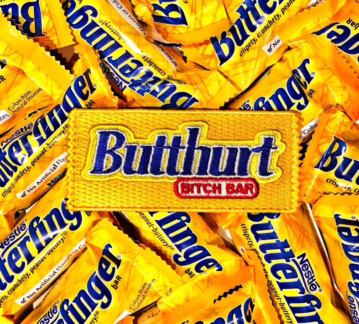 Yellow candy bar shaped embroidered patch with text in blue that reads Butthurt bitch bar
