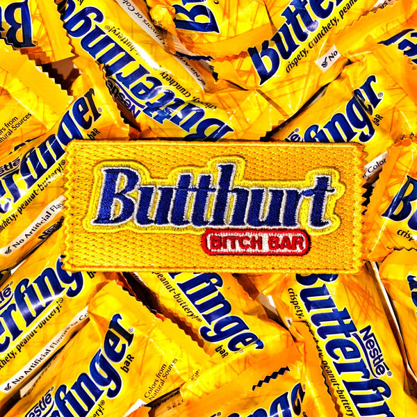 Yellow candy bar shaped embroidered patch with text in blue that reads Butthurt bitch bar