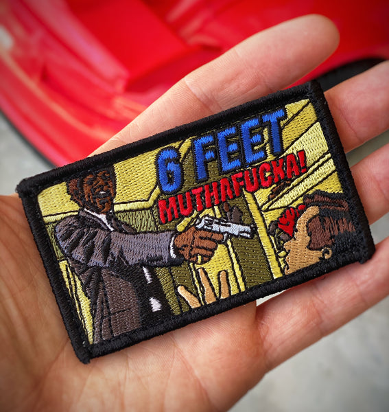Embroidered rectangle shaped patch depicting a man holding a gun with text that reads 6 feet muthafucka