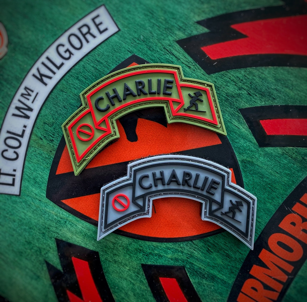 One grey and one green Ranger tab shaped patch with the word Charlie in the center followed by a red circle with a slash on one side and a silhouette of a surfer on the other 