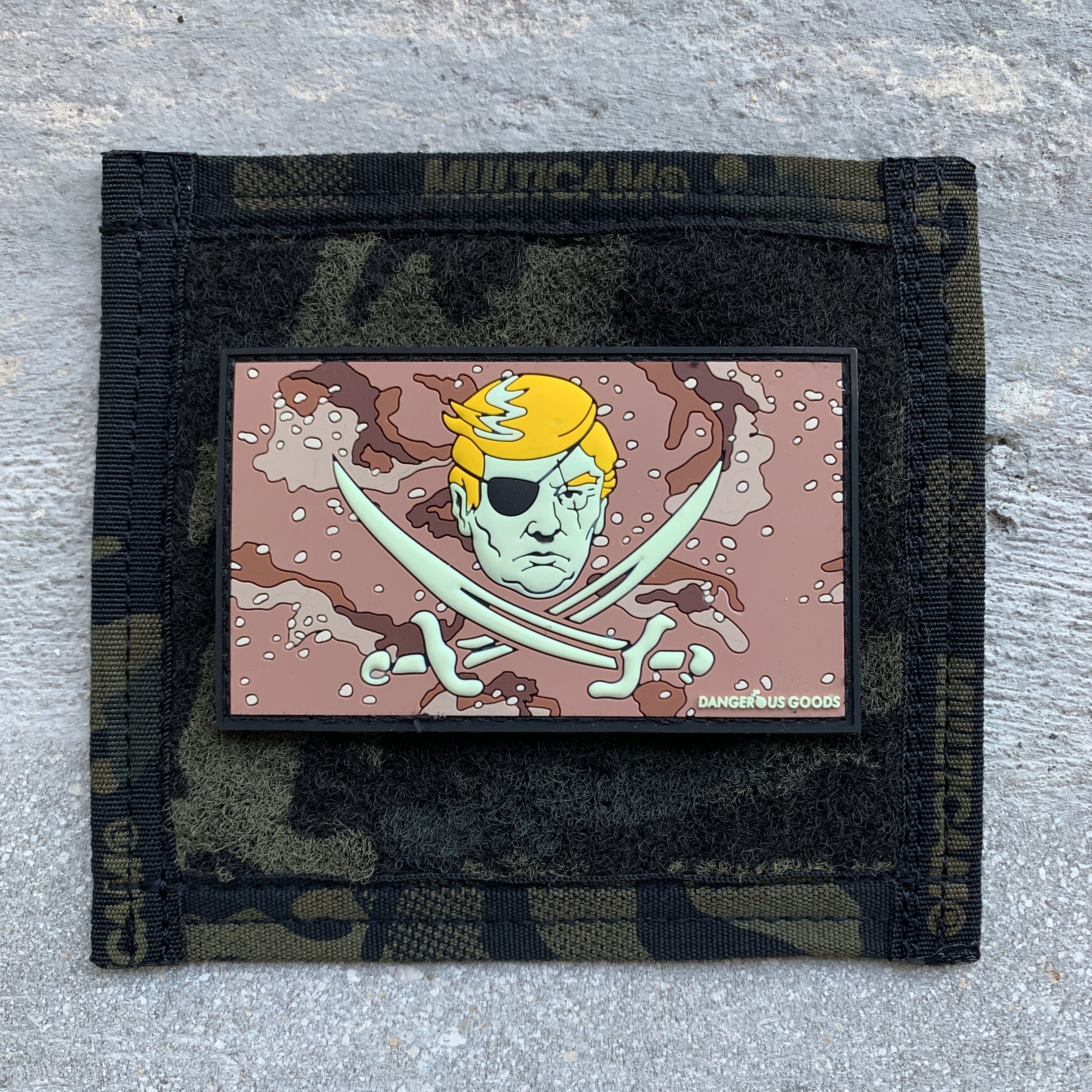 Tan desert storm style camo pvc rubber patch depicting a cartoon image of trumps head with two crossing pirate swords underneath 