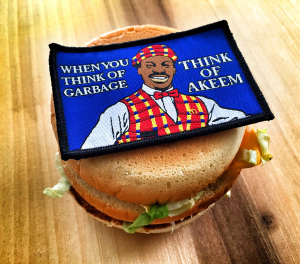 Embroidered patch of man smiling wearing fast food worker uniform with text that reads When you think of garbage think of akeem